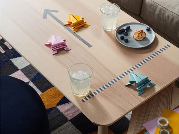 Konferenčný stolík s taniermi a pohármi s občerstvením a pretekárskou dráhou s modelmi z papiera na origami LUSTIGT.