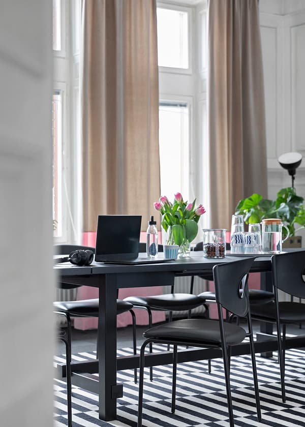 Konferensrum med stora fönster, beige och rosa gardiner, svart rektangulärt bord med svarta stolar  på IKEA STOCKHOLM svartvit matta.