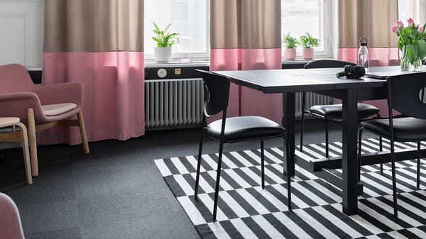 Konferensrum med stora fönster, beige och rosa gardiner, svart rektangulärt bord med svarta stolar  på IKEA STOCKHOLM svartvit matta.