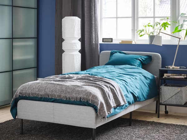 コンパクトなベッドにブルーの寝具を合わせたモダン寝室。グレーの壁と白い装飾で洗練された空間。