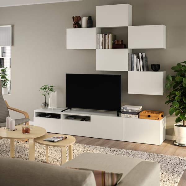 Konsol TV dengan pintu berwarna putih BESTÅ yang mempunyai TV besar di atasnya serta kabinet bermodul BESTÅ yang terlekap pada dinding, terletak di ruang tamu. 