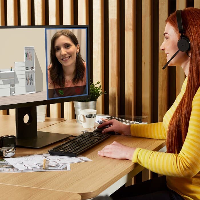 Konsultantka IKEA siedzi przed ekranem komputera, na ekranie widać projekt regału oraz klientkę w trakcie wideorozmowy.