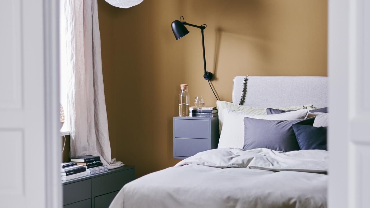 Koselig soverom med vegger i varm beige og DUNVIK kontinentalseng, vegglampe og nattbord.