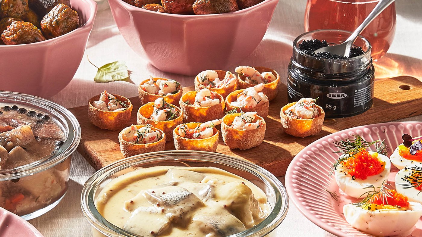Košíčky KRUSTADER s krevetami a kaviár SJÖRAPPORT sú položené na doske na krájanie, vedľa toho sú misky s nakladanými sleďmi a guľôčkami a tanier s vajíčkami ozdobenými kaviárom.