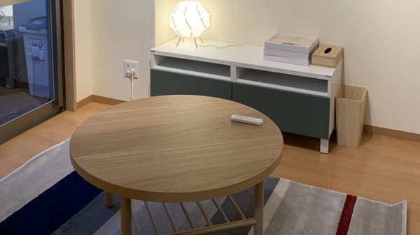 カーペットが敷かれ、円いローテーブルが置かれている。チェストの上に間接照明が置かれている。