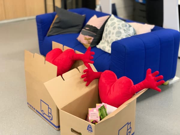 Krabice IKEA s červenými srdíčky a dalšími výrobky, za nimi stojí modré křeslo KLIPPAN.