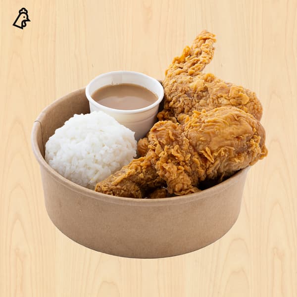 Kraft-paper bowl of crispy fried chicken, white rice, and dipping sauce on a wood table; warm, appetizing meal with golden textures.
