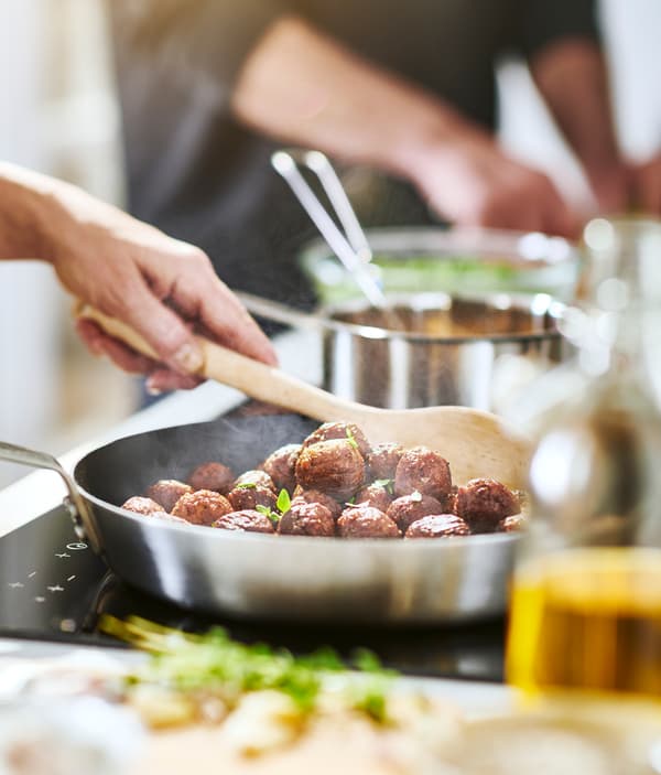 كرات نباتية HUVUDROLL من ايكيا يجري طهيها في قدر من الصلب المضاد للصدأ ومزجها باستخدام ملعقة خشبية.