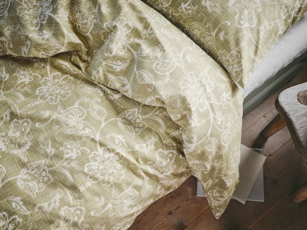 Krevet s IKEA JUNIMAGNOLIA posteljinom od pamuka s klasičnim uzorkom bijelo-zelenog cvijeća.