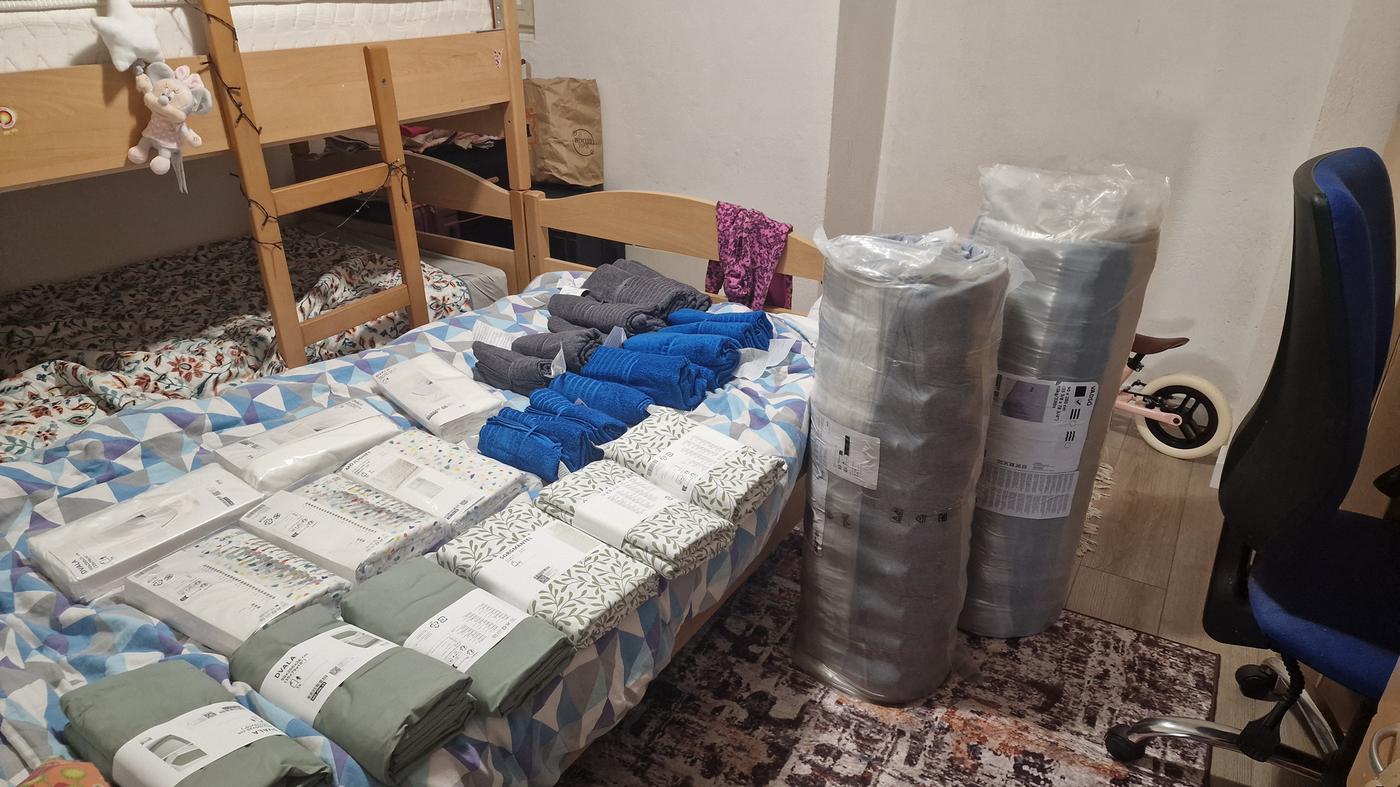 Krevet s posteljinom i ručnicima, uz dva velika smotuljka madraca.