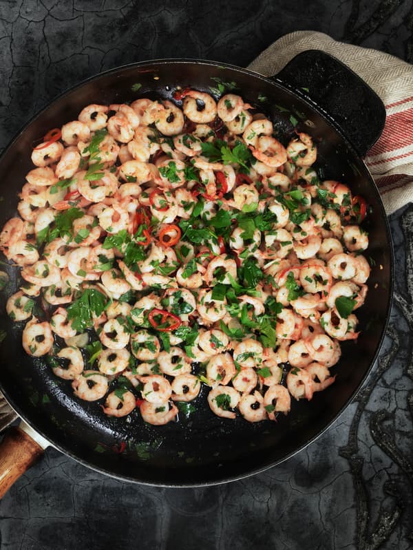 Krevety SJÖRAPPORT s petrželovou natí a chilli papričkami v litinové pánvi.