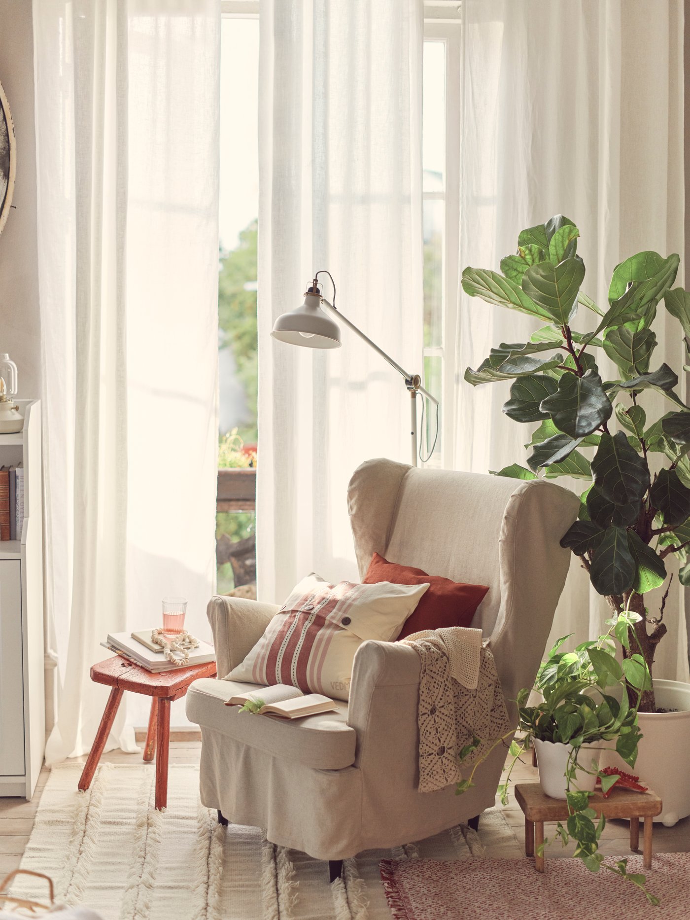 كرسي بظهر مرتفع وجوانب بارزة STRANDMON على الطراز التقليدي بغطاء إنزلاقي من الكتان الطبيعي، وعليه وسائد وأغطية بجانب نباتات بآنية نباتات.