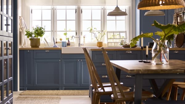 Kuchnia METOD z frontami w kolorze niebieskim LERHYTTAN ma duże okna, wyspę kuchenną z szufladami i stół jadalny.