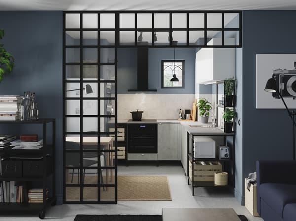 Kuchnia narożna z otwartymi i zamkniętymi szafkami w kolorze antracytowym, białym i imitującym beton, czarnymi lampami, ziołami w doniczkach i jutowym dywanem.