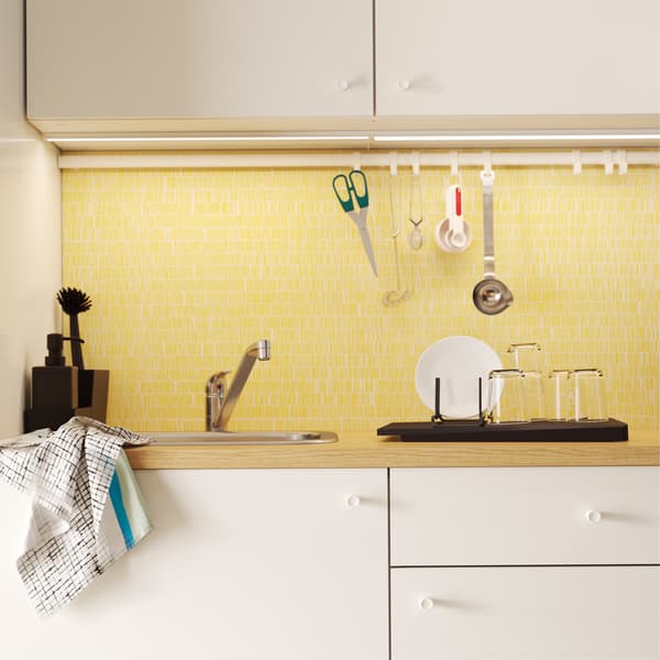 Kuchnia z białymi drzwiami, żółtym panelem i drążkiem z haczykami, na których zawieszono nożyczki i inne akcesoria.