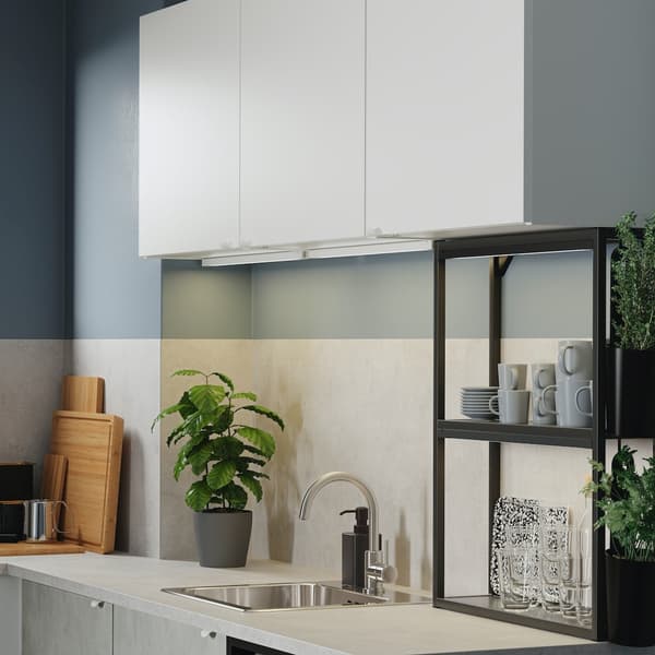 Kuchnia z białymi szafkami, antracytowymi otwartymi półkami, frontami imitującymi beton, ocynkowaną baterią i LED-ową listwą oświetleniową.