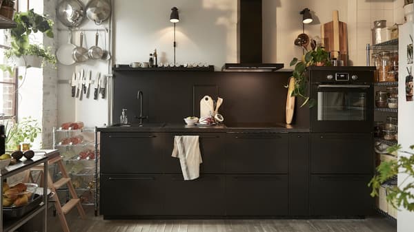 Kuchyňa s čiernymi dvierkami IKEA KUNGSBACKA, vozíkom z nehrdzavejúcej ocele a dvomi čiernymi nástennými lampami.