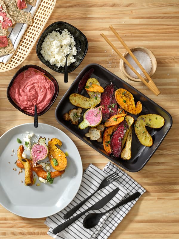 Kuchynská pracovná doska so sivým okrúhlym tanierom FORMIDABEL a farebným jedlom na čiernych servírovacích tanieroch. 