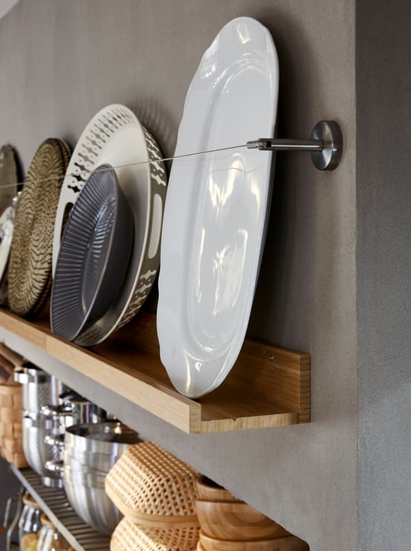 Kuchynské nástenné úložné priestory s drevenou policou na obrazy MÅLERÅS s taniermi z kameniny, podnosmi a ďalšími kuchynskými doplnkami. 