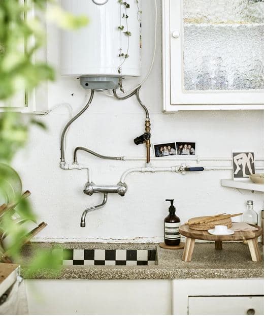 Kuchynský drez s bojlerom, zatvorené skrinky a drevený servírovací riad v malej osobnej kuchyni.