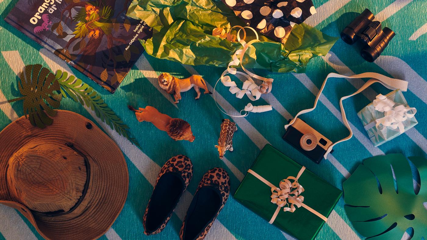 Különböző becsomagolt és doboz nélküli ajándékok és játékok a felfedezés és kaland témája mentén egy GRACIÖS szőnyegen.