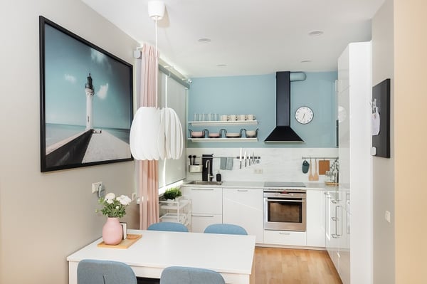 Кухня и обеденная зона в скандинавском стиле с белой мебелью, синими стульями и настенным декором

