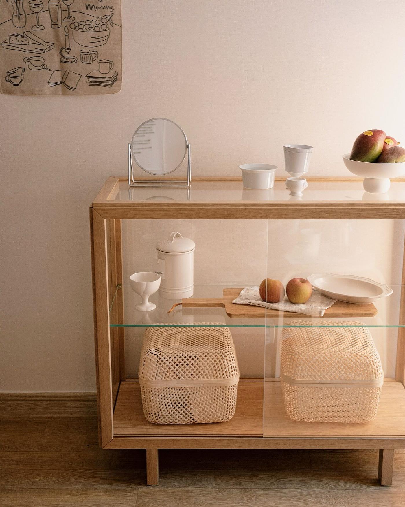 Kundbild från @6.0ee av ett minimalistiskt STOCKHOLM 2025 vitrinskåp i trä och glas med vit keramik, färsk frukt och flätade förvaringskorgar.