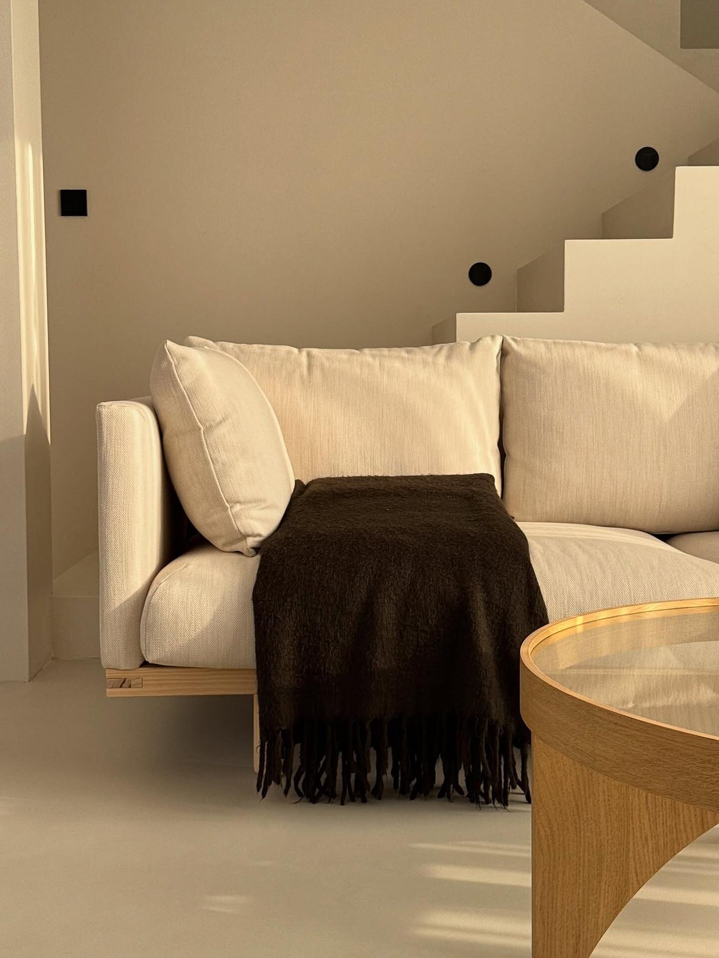 Kundbild från @patrycja.brylka på en beige STOCKHOLM 2025 soffa med en mörkbrun pläd i ett modernt, minimalistiskt vardagsrum med ett soffbord i trä.