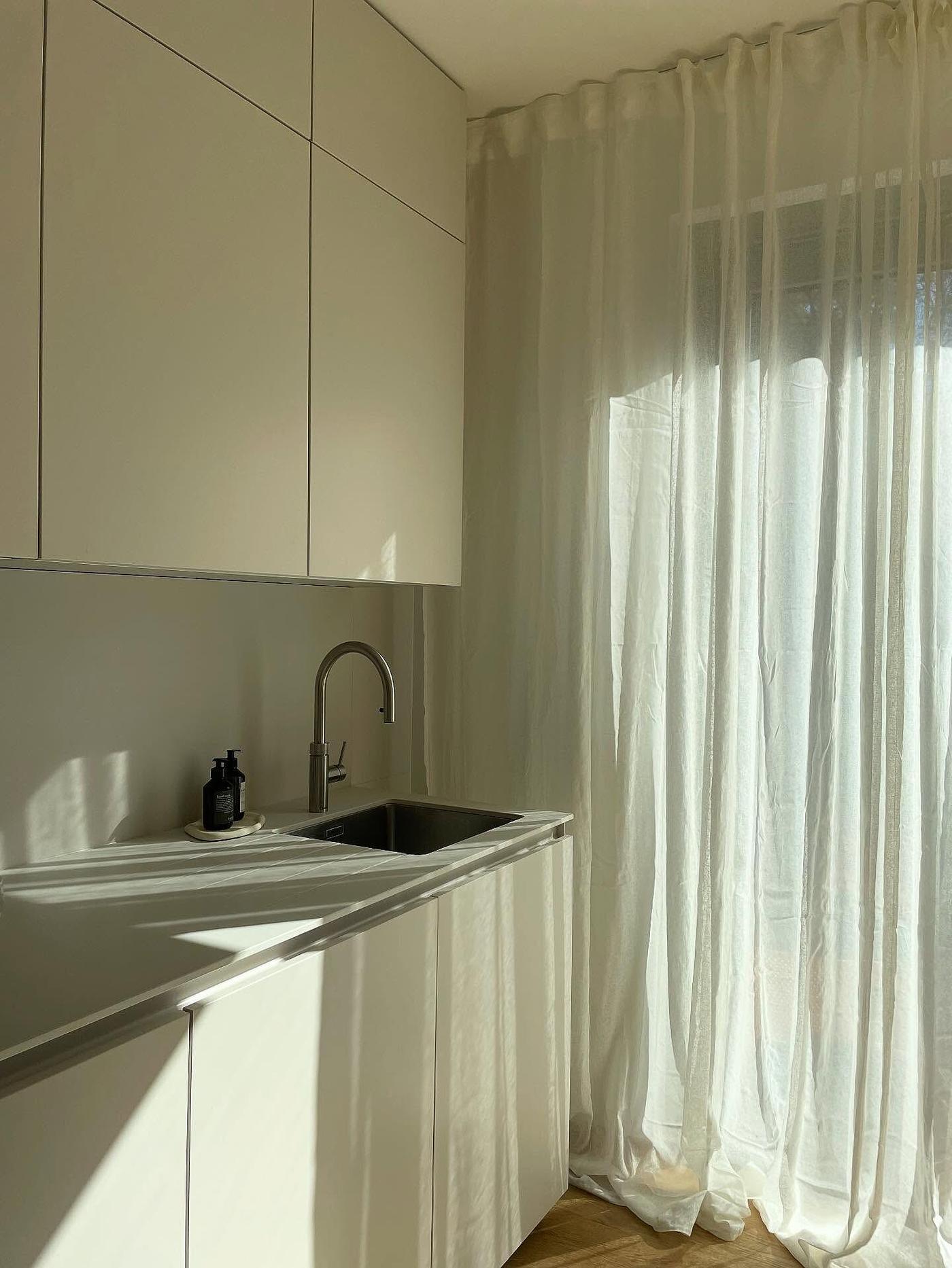 Kundbild från @studio.ohlola på solljus som strömmar in genom skira vita STOCKHOLM 2025 gardiner i ett modernt grovkök med stilrena vita skåp och en infälld diskho.