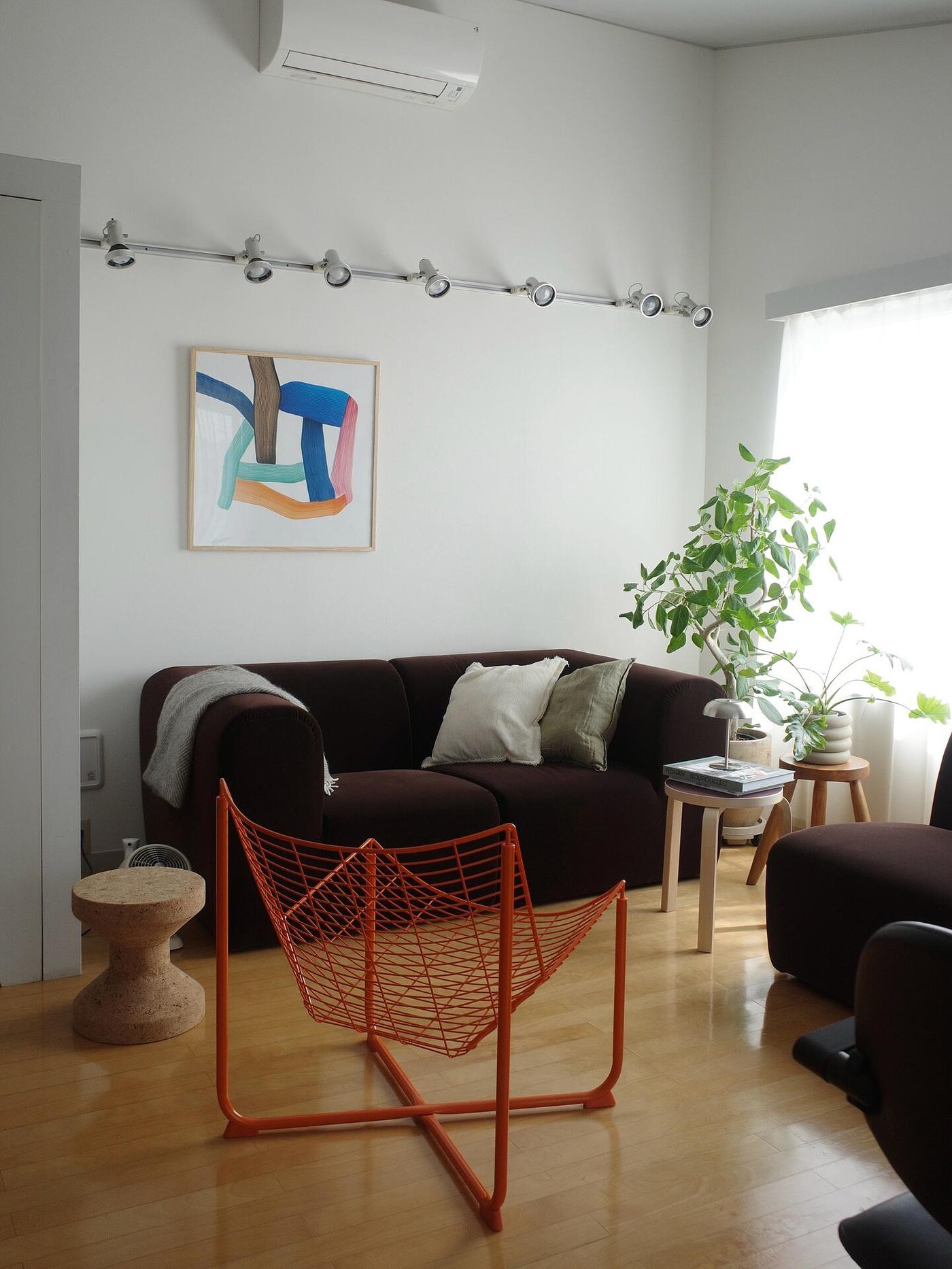 Kundbild från @tomo_room00 på ett modernt vardagsrum med en mörkbrun STOCKHOLM 2025 soffa, ett orange tidningsställ i nätdesign och ett färggrant, abstrakt konstverk på väggen.