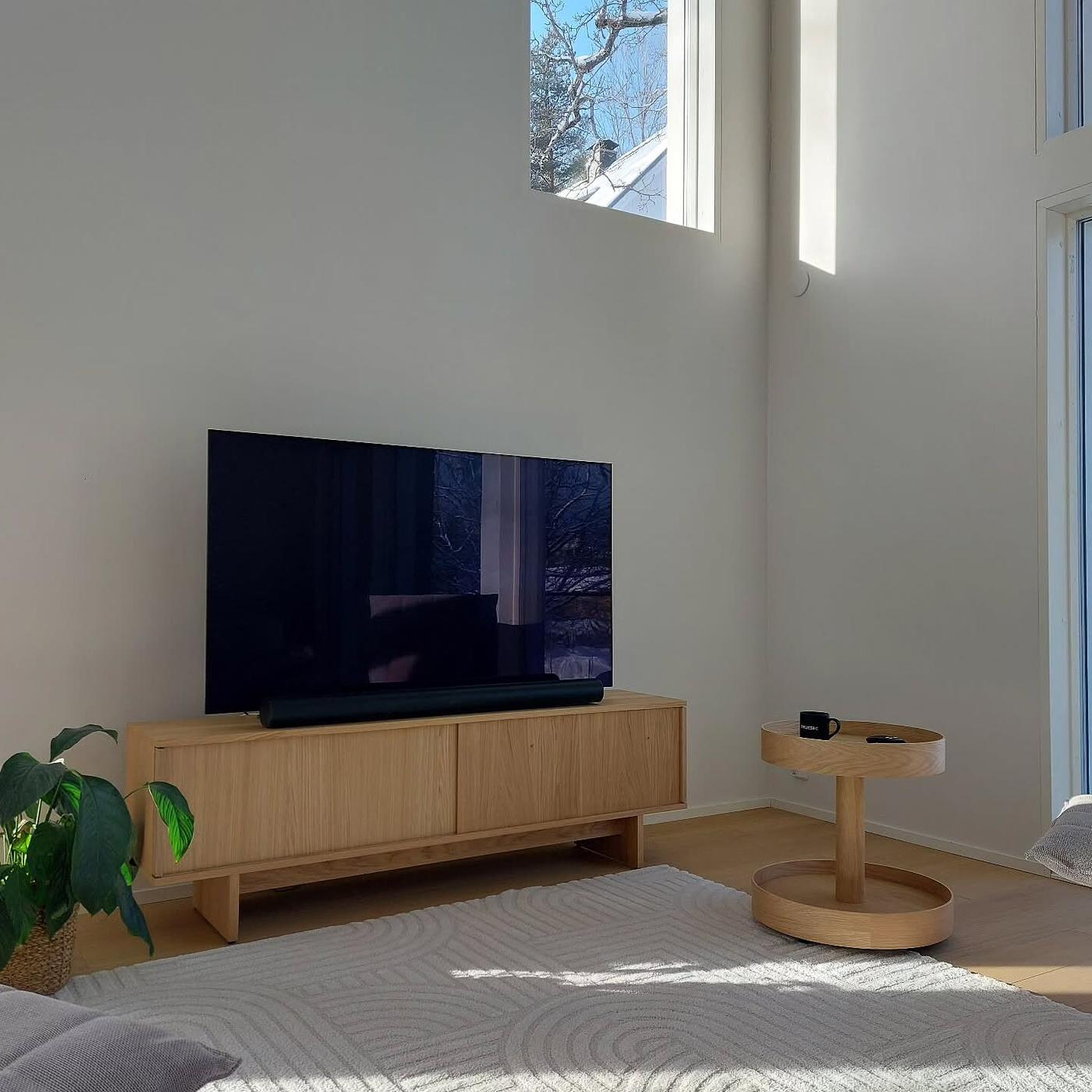 Kundbild från @villasimolinLjust av ett modernt vardagsrum med en TV på en STOCKHOLM 2025 mediamöbel i trä, ett runt sidobord och en ljus matta i ett solbelyst rum.