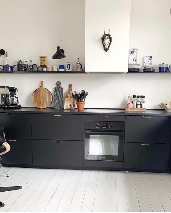 Kundbild på kök med svarta skåp, svart bänkskiva, hylla med köksprylar, inbyggd ugn och dekorskalle på väggen.