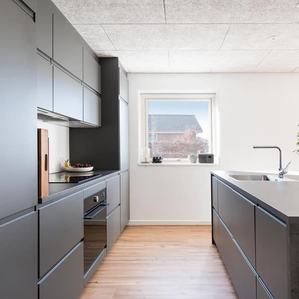 Kundbild på modernt kök med grå skåp, ljust trägolv, stora fönster, inbyggda vitvaror och minimalistisk design.