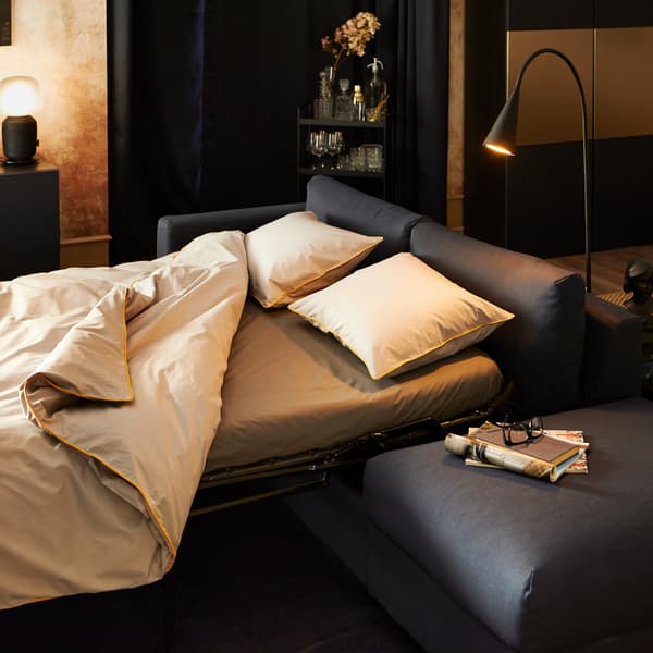 KUNGSBLOMMA quilt cover and 2 pillowcases in grey and yellow on a sofa bed, with lamps and a display cabinet to the rear.