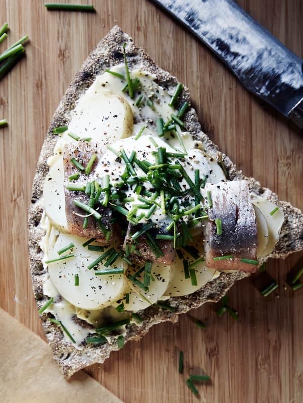 Kus chrumkavého chleba KNÄCKEBRÖD RÅG obloženého plátkami uvarených zemiakov, kúskami marinovaného sleďa SILL MATJES a pažítkou.