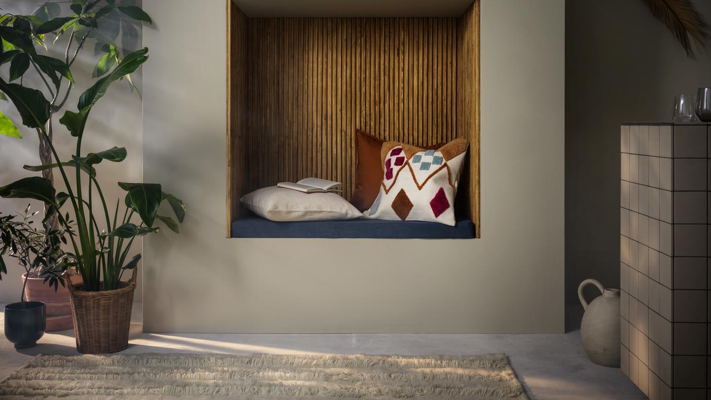 Kútik na čítanie s vankúšmi, vedľa toho na jednej strane rastliny v kvetináčoch, na druhej strane keramická váza.