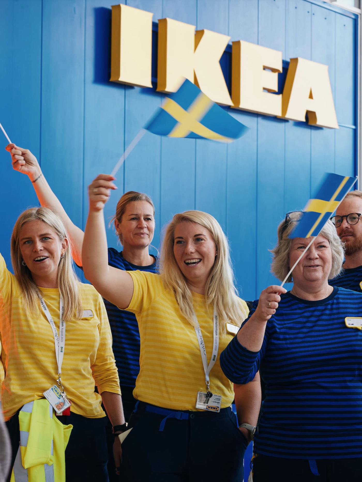 Kvindelige IKEA medarbejdere flager med det svenske flag foran et IKEA varehus.