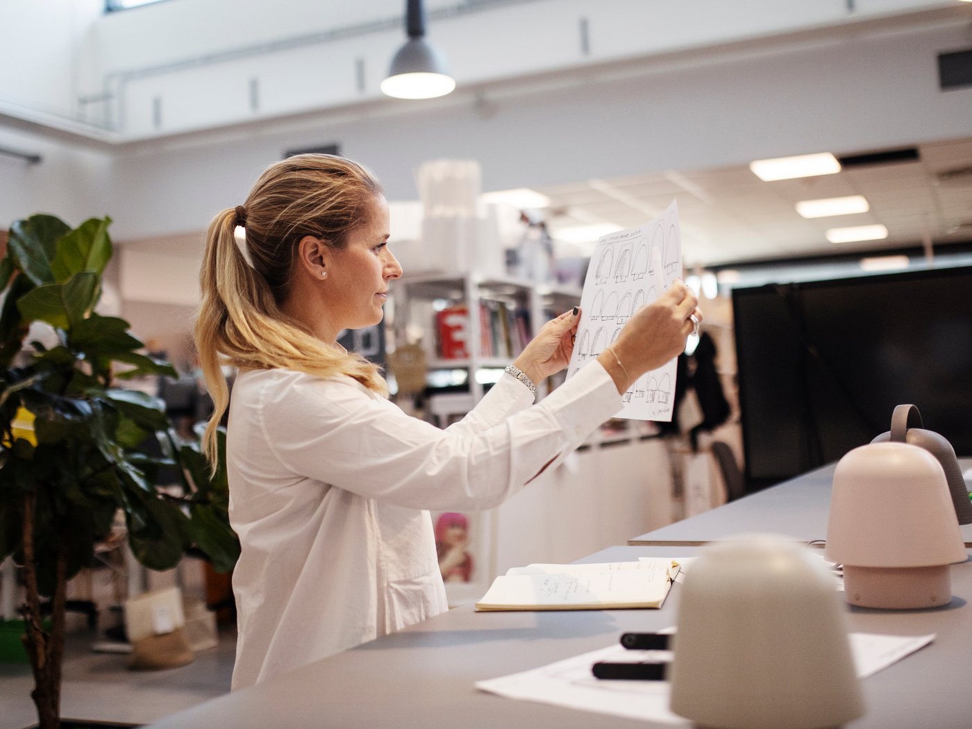 Kvinna i vit skjorta står i en öppen lokal och granskar en vit ritning som hon håller upp