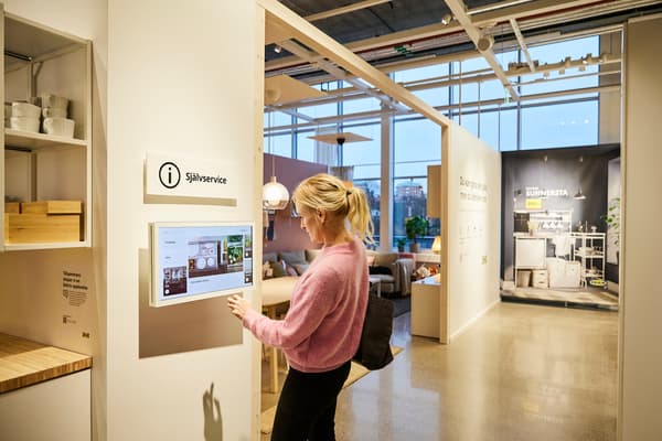 kvinna med rosa tröja och blont hår tittar på en skärm där det ovan står "Självservice"