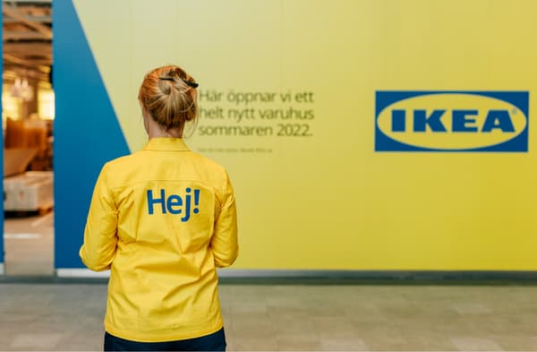 Kvinna med  texten "Hej!" på ryggen tittar på gul vägg med IKEA-logga