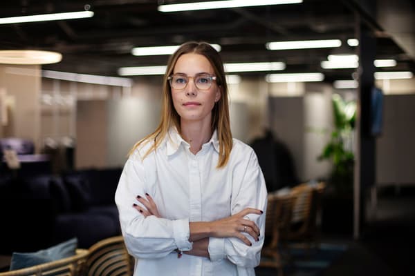 Kvinna med vit skjorta och glasögon tittar mot kameran