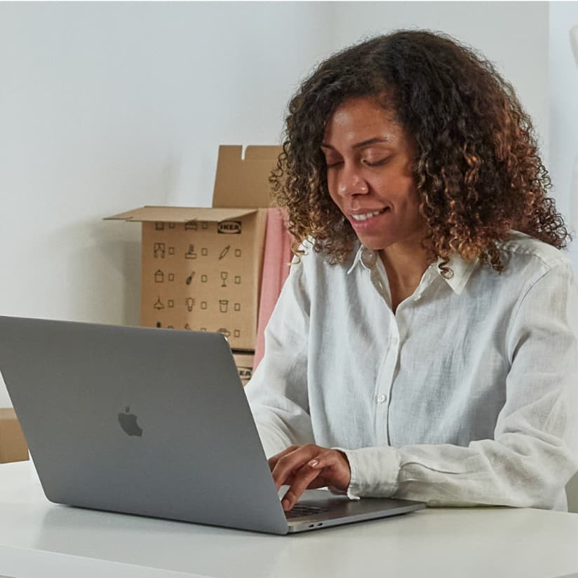 Kvinna som sitter framför sin laptop hemma vid sitt köksbord. 