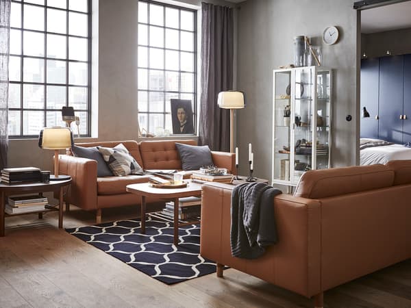 キャメル色のレザーソファを並べたモダンリビング。大きな窓と幾何学柄ラグで開放感を演出。