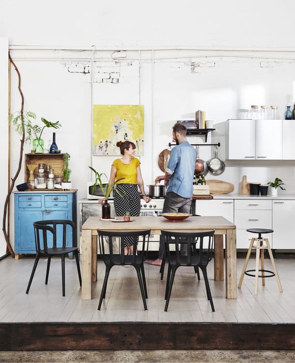 Kyra et Dave dans leur cuisine blanche meublée d’une table en bois et de chaises noires.