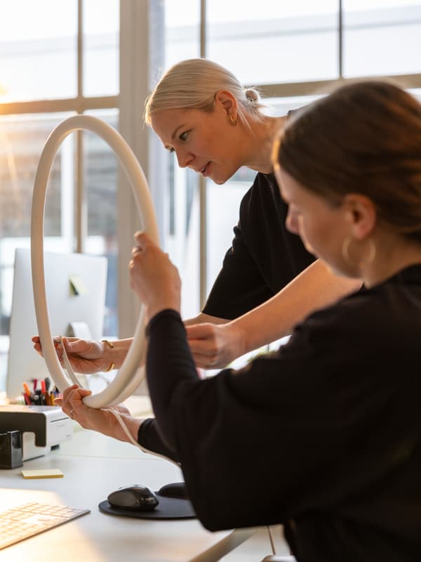 La designer Sabine Marcelis examine le prototype d’une applique circulaire VARMBLIXT avec son assistante dans son studio de Rotterdam.