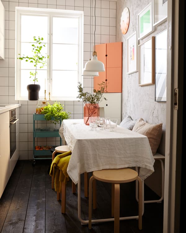 La même petite cuisine aménagée pour recevoir, avec une table dressée, un banc et des tabourets empilables.