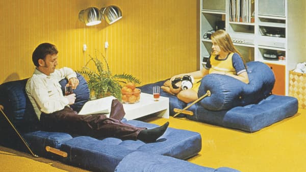 La photo de couverture du catalogue IKEA de 1973 montre un couple allongé sur deux fauteuils/relax TAJT dans une pièce à moquette jaune.