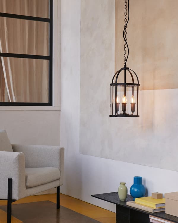 La tradizionale lampada a sospensione GALJON, con tre lampadine decorative accese, accanto a una poltrona e un tavolino.
