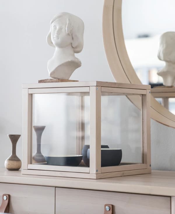 La vitrine SAMMANHANG accueille une collection de bols en céramique noire ainsi qu’un buste, le tout sur la commode en bois clair.
