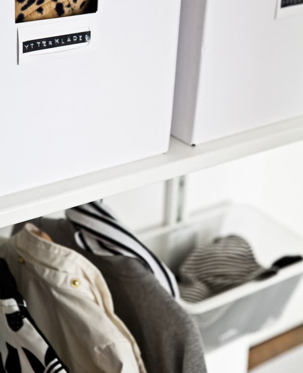 Labelled white boxes on a shelf above a hanging rail.